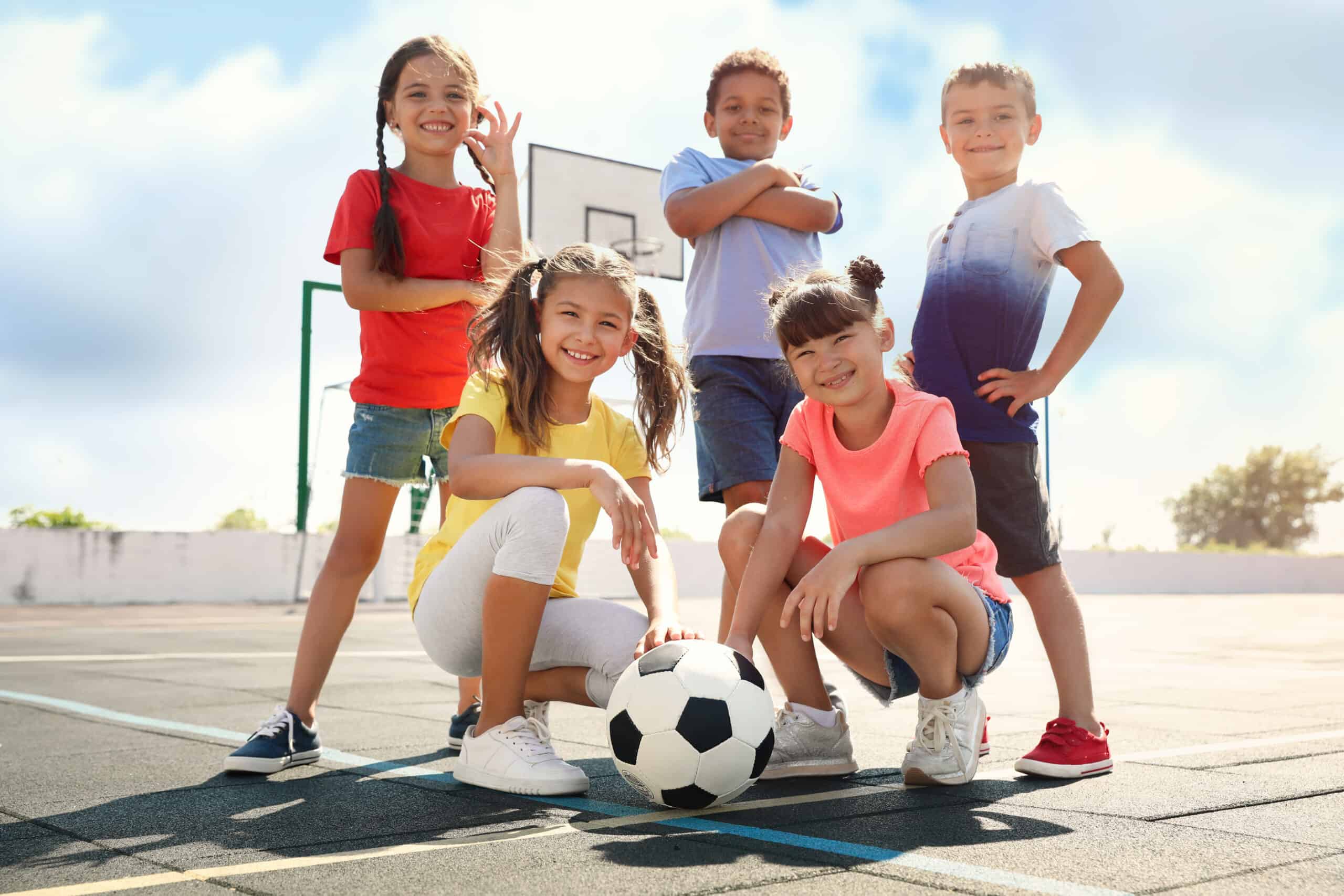 Cute children with soccer ball at sports court on sunny day. Summer camp