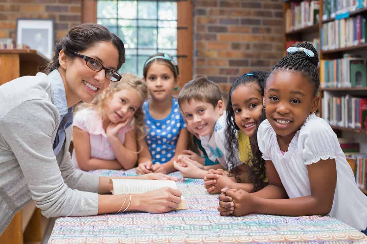 Cute pupils and teacher reading in library at the elementary school