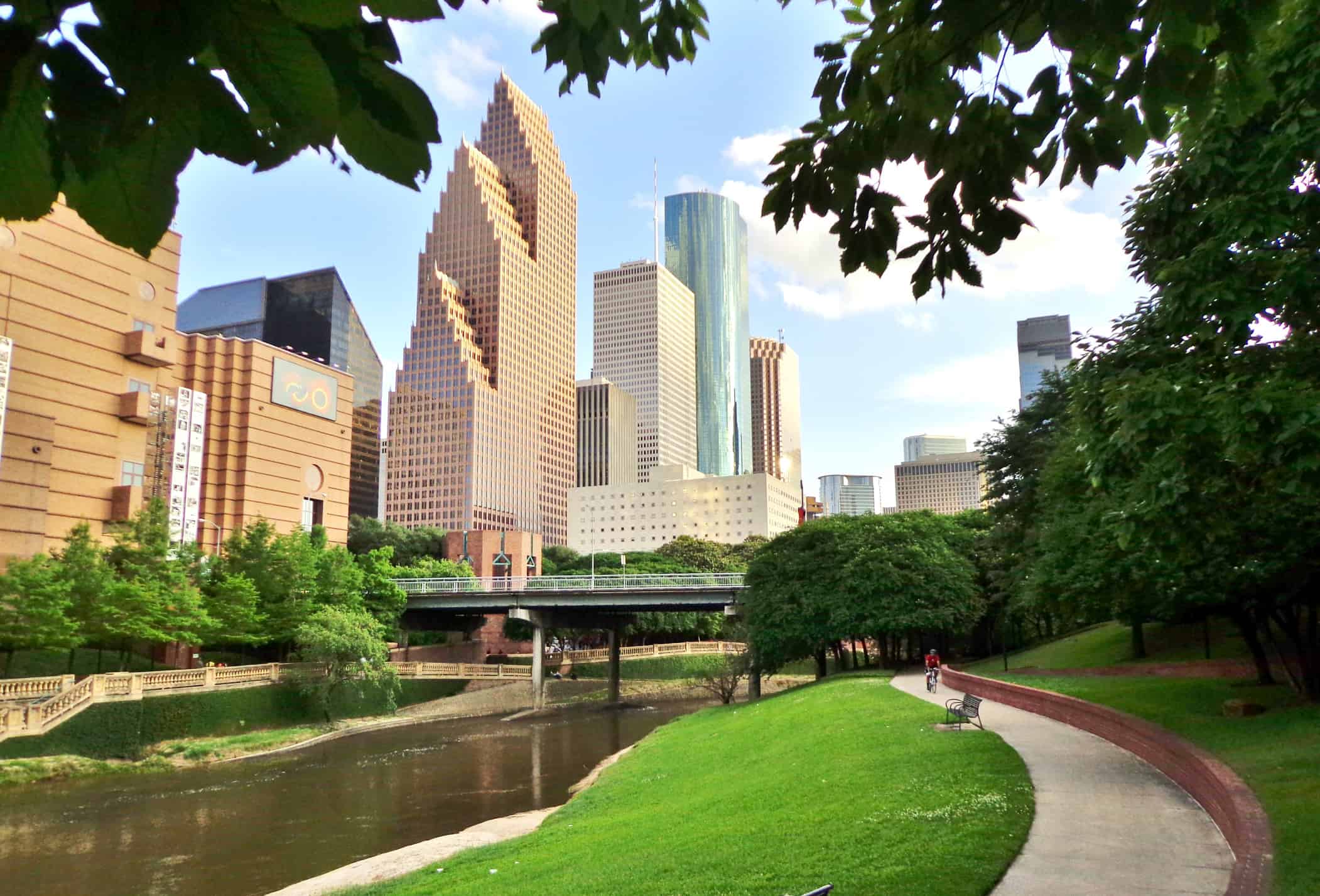 Wide shot of Houston's modern skyline and paved bicycle/walking path in Buffalo Bayou Park on a summer afternoon