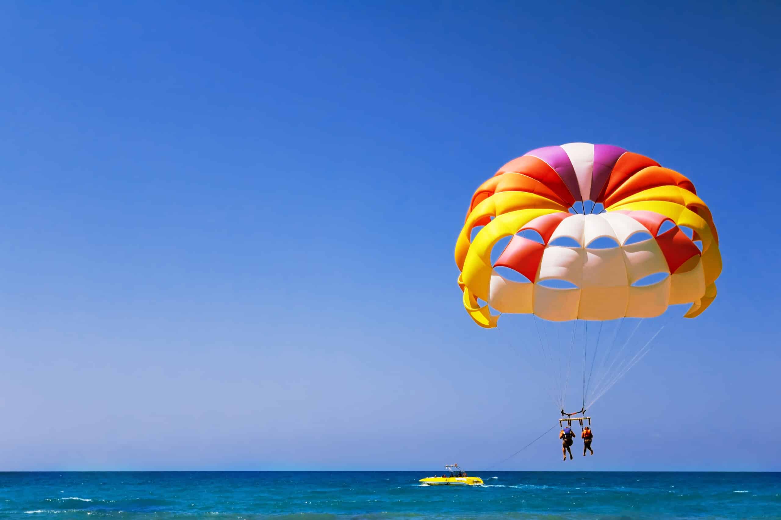 A large parachute with two girls flies in the air over the sea."n