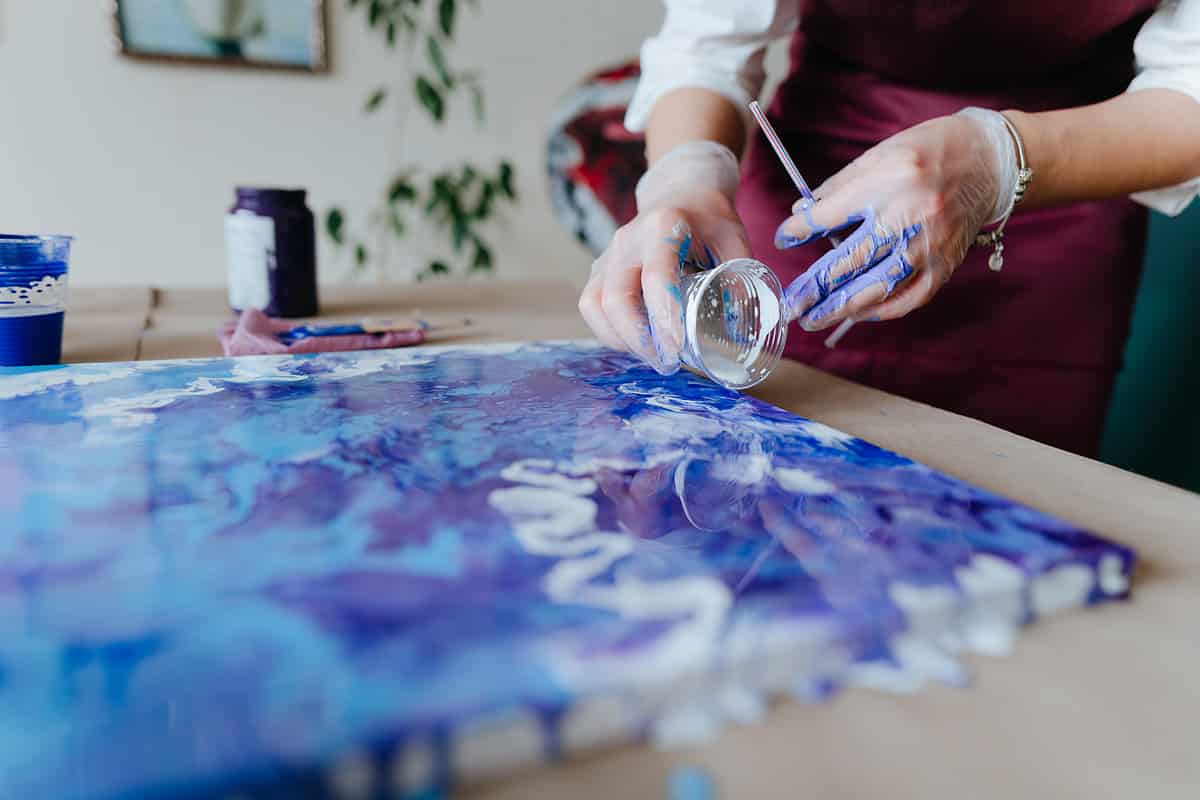 Female artist mixing acryl paints on the picture working in fluid art technique. Selective focus.