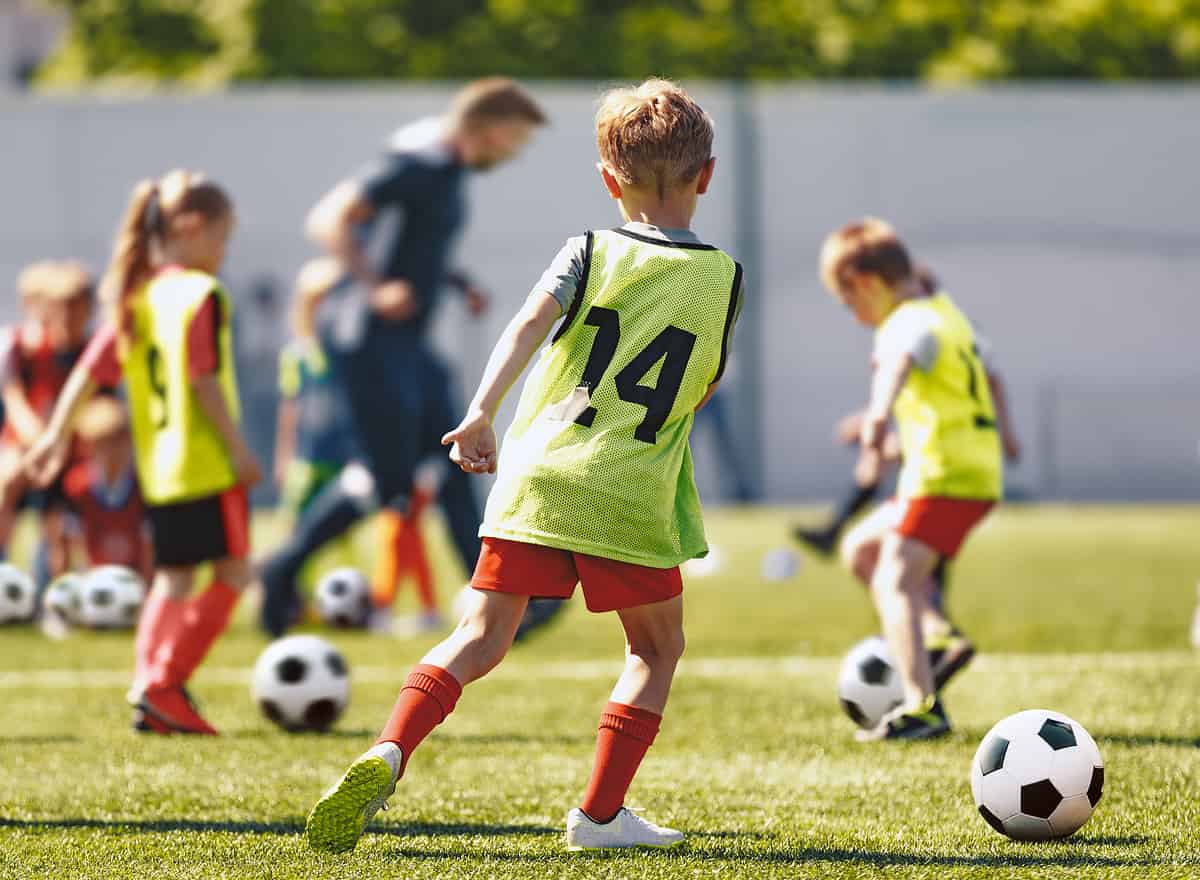 School Children Play Soccer Football Training Game With Coach. Kids Kicking Sports Balls on Grass Field. Football Practice For Youth