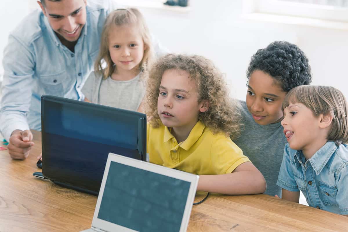 Young children working together on a laptop, trying to solve a programming question with their teacher