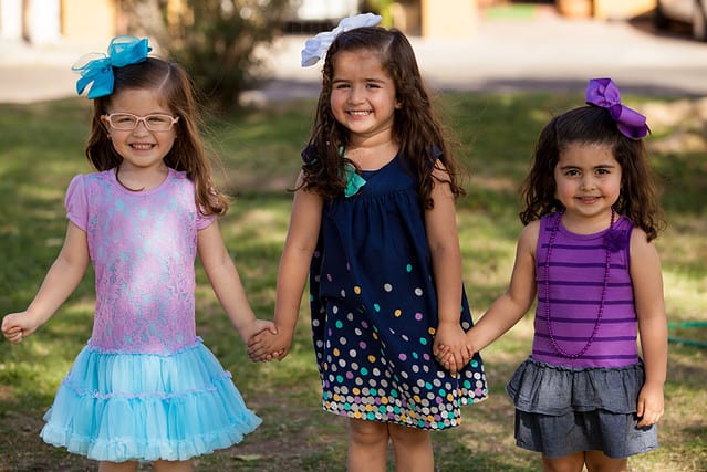 Portrait of three little girls smiling and holding hands in a park on a sunny day