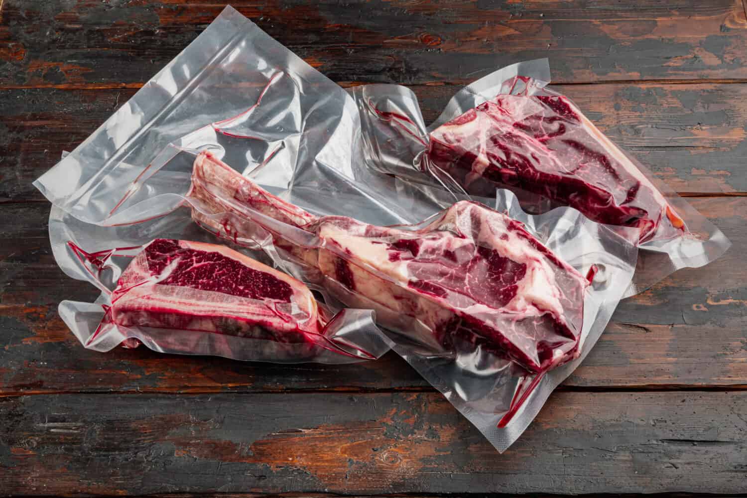 Dry aged steak in a vacuum marbled beef meat pack set, tomahawk, t bone and club steak cuts, on old dark wooden table background