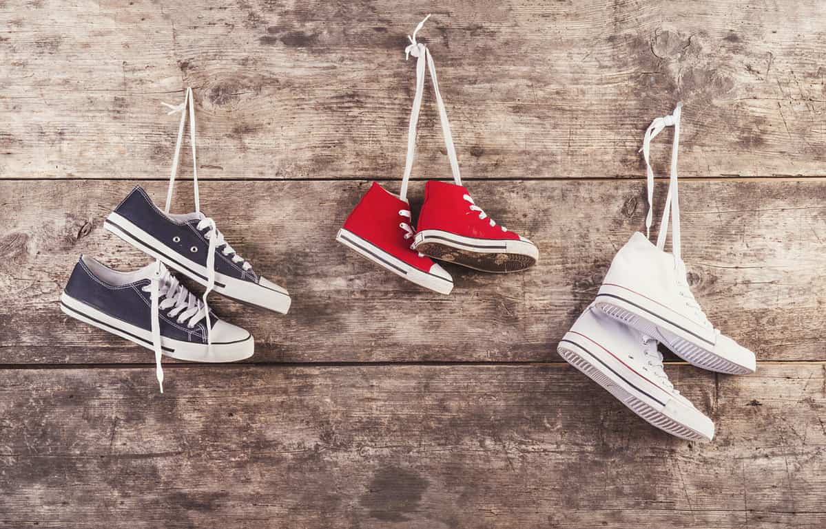 Three pairs of sports shoes hang on a nail on a wooden fence background