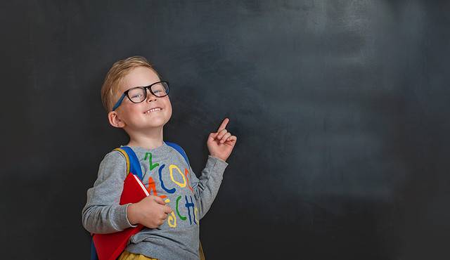 Back to school. The funny little boy in glasses pointed up at the blackboard. Child from elementary school with book and bag.