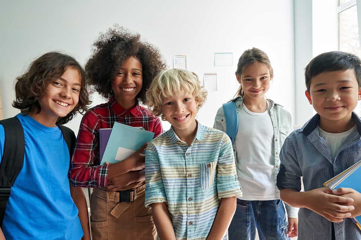 Happy diverse junior school students group looking at the camera standing in the classroom. Smiling multiethnic cool kids boys and girls friends posing for group portrait together.