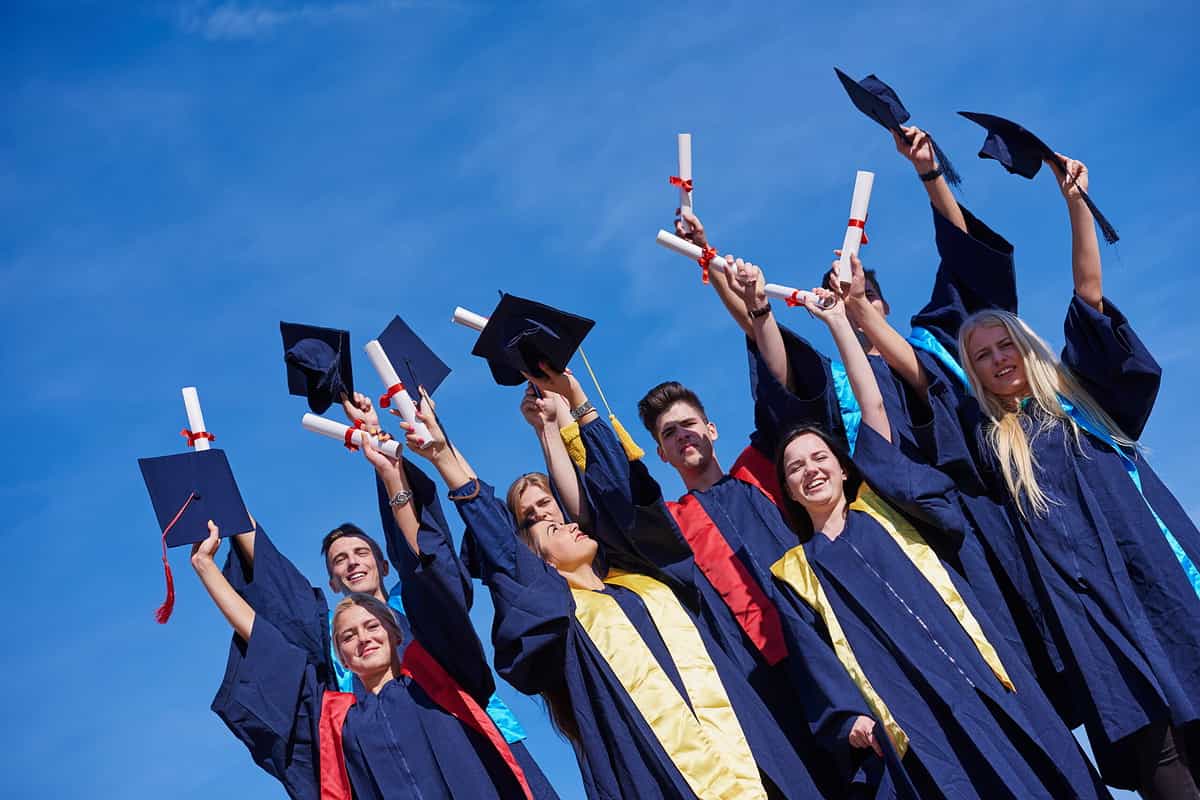 high school students graduates tossing up hats over blue sky.