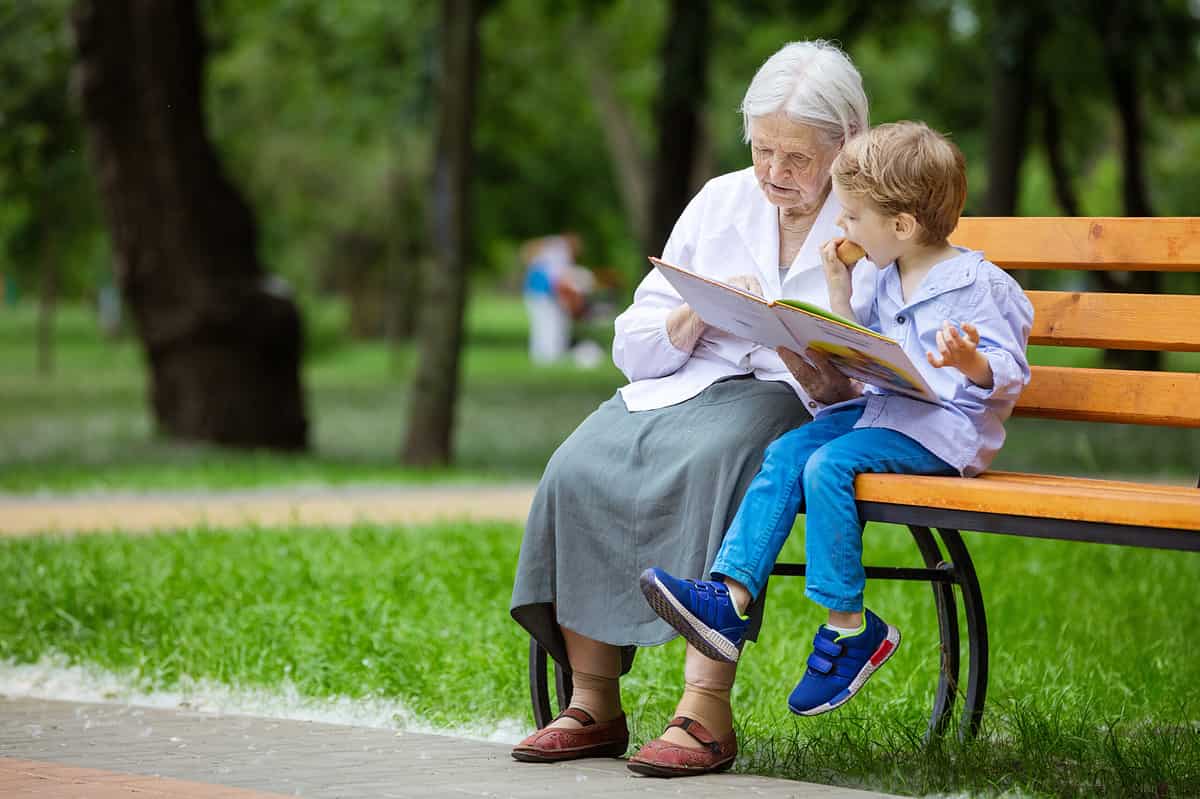 great grandma and grandson sitting in a park reading a book