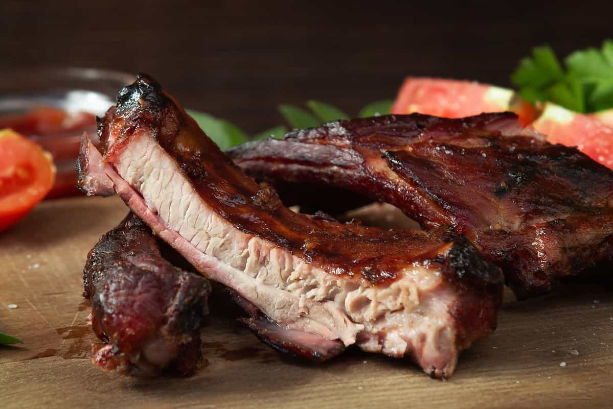 Sliced into pieces barbecue pork ribs on a wooden cutting board with vegetables.