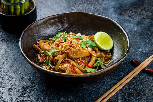 pad thai noodles with chicken on dark stone table