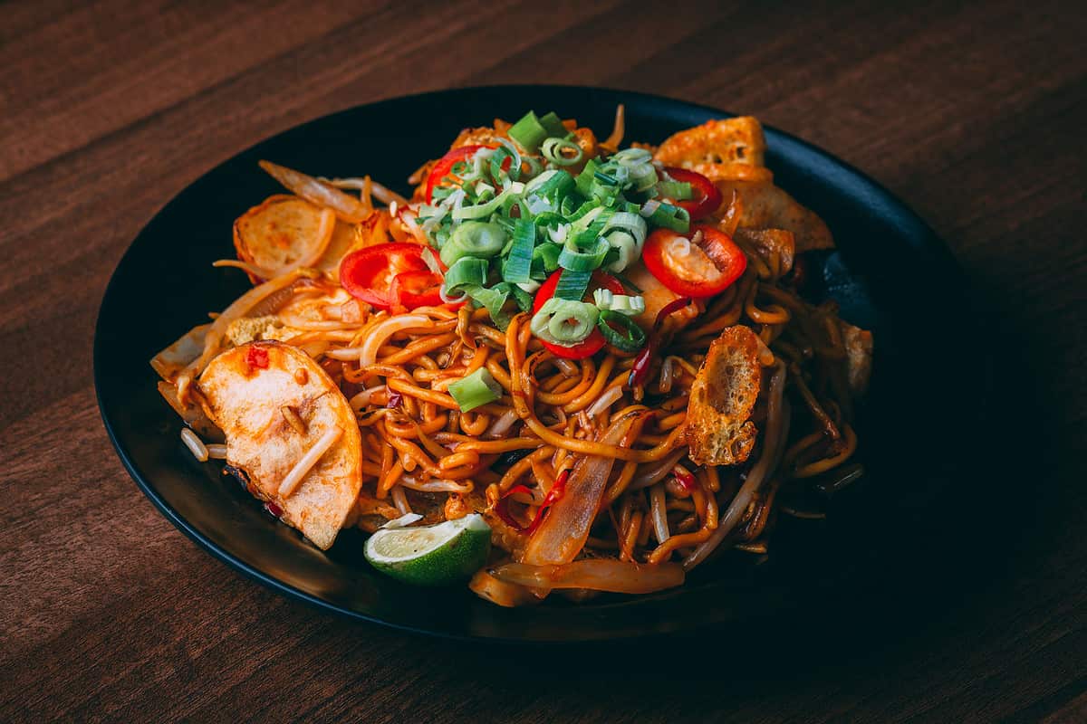 A closeup shot of Chinese lo mein noodles topped with red pepper and sliced green onion