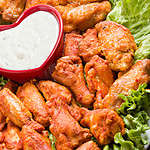 "A high angle close up of a plate full of Buffalo wings with a red, heart shaped bowl full of blue cheese dipping sauce."