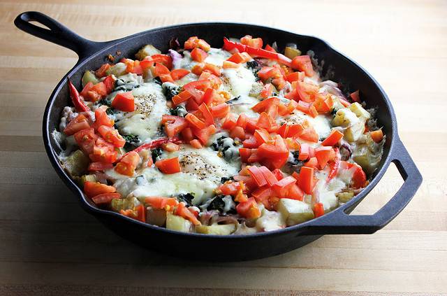 A hearty spinach nest and tomato skillet breakfast set on a wooden surface