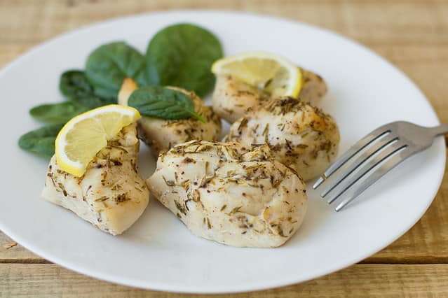 Baked chicken fillet with lemon slices and spinach leaves on a white simple plate