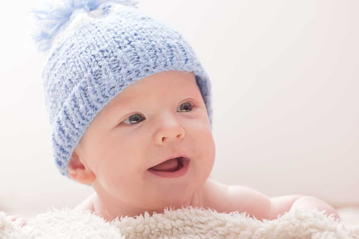 A newborn baby in blue hat smiling.