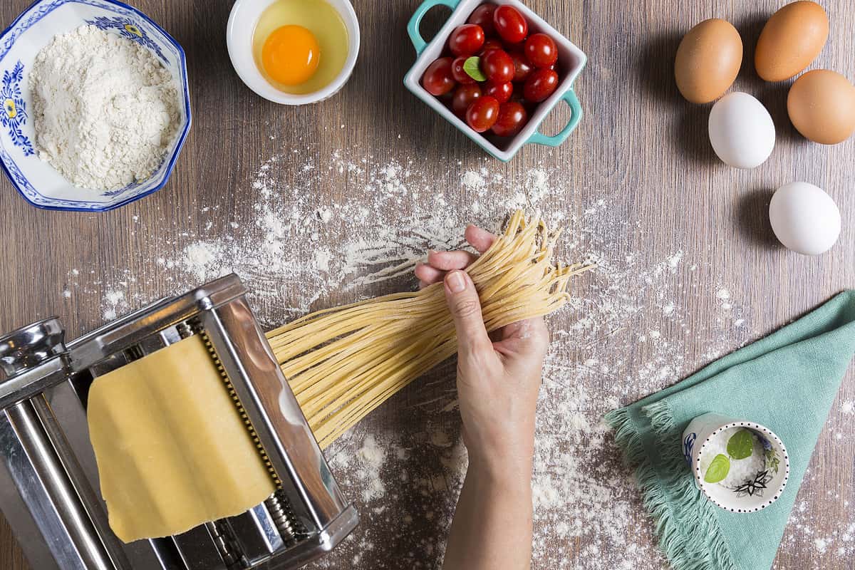 Making homemade pasta noodles with pasta maker with some ingredients around.