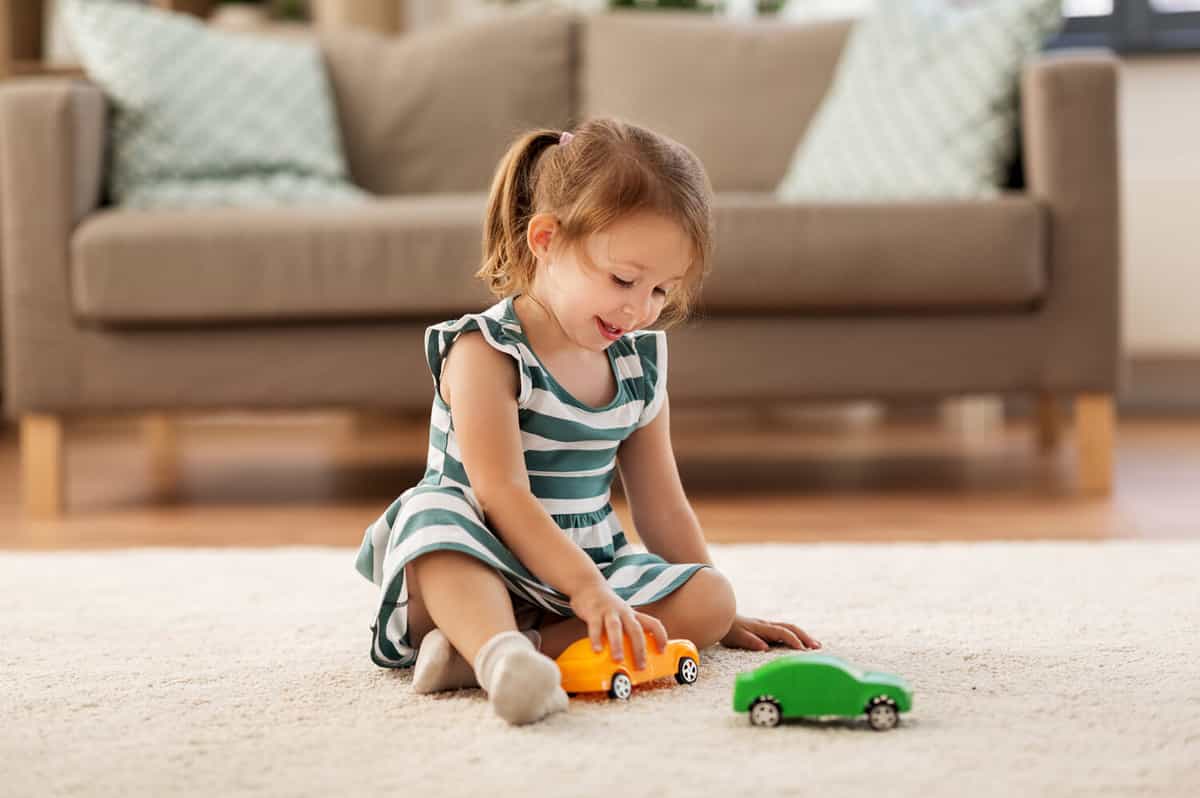 childhood and people concept - happy three years old baby girl playing with toy car at home