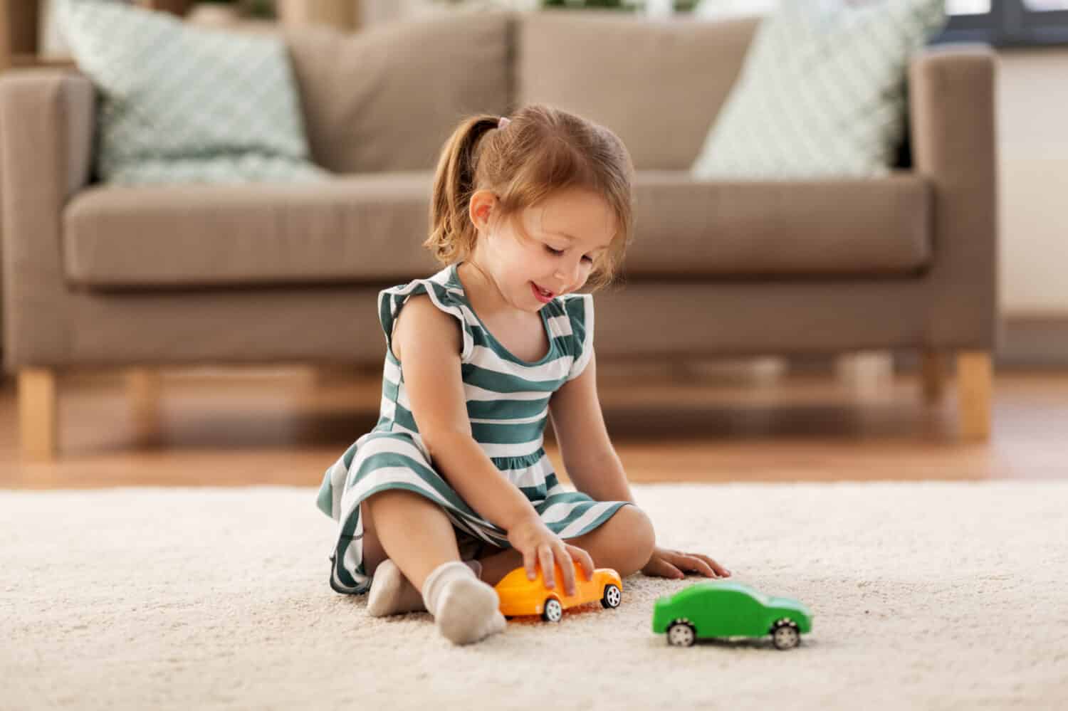 childhood and people concept - happy three years old baby girl playing with toy car at home