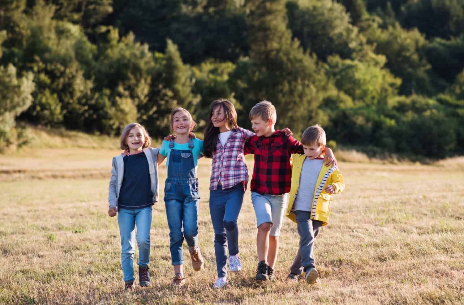 Group of school children walking on field trip in nature, arm in arm.