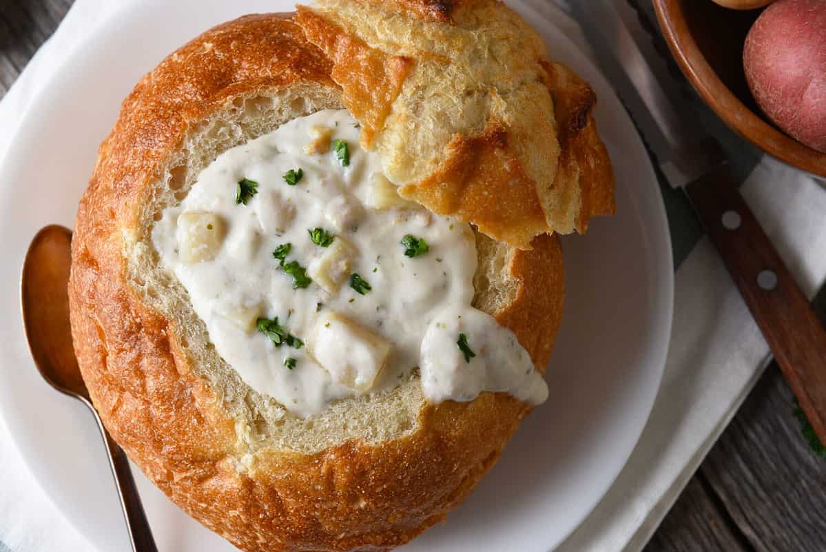 High angle closeup of a bread bowl of New England Style Clam Chowder on a rustic wood table.