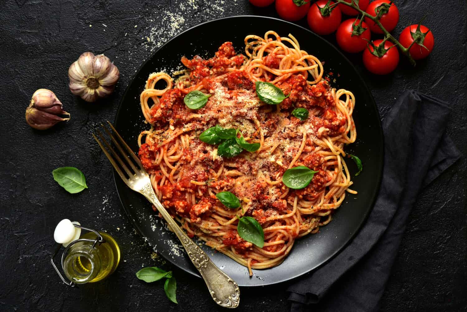 Traditional italian spaghetti bolognese on a black plate on a dark slate, stone or concrete background. Top view with copy space.