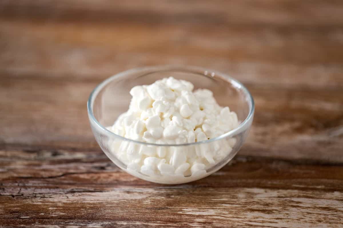 food and dairy products concept - close up of homemade cottage cheese in glass bowl on wooden table