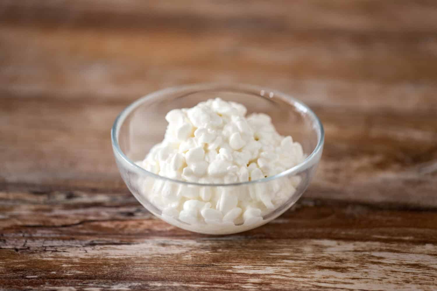 food and dairy products concept - close up of homemade cottage cheese in glass bowl on wooden table