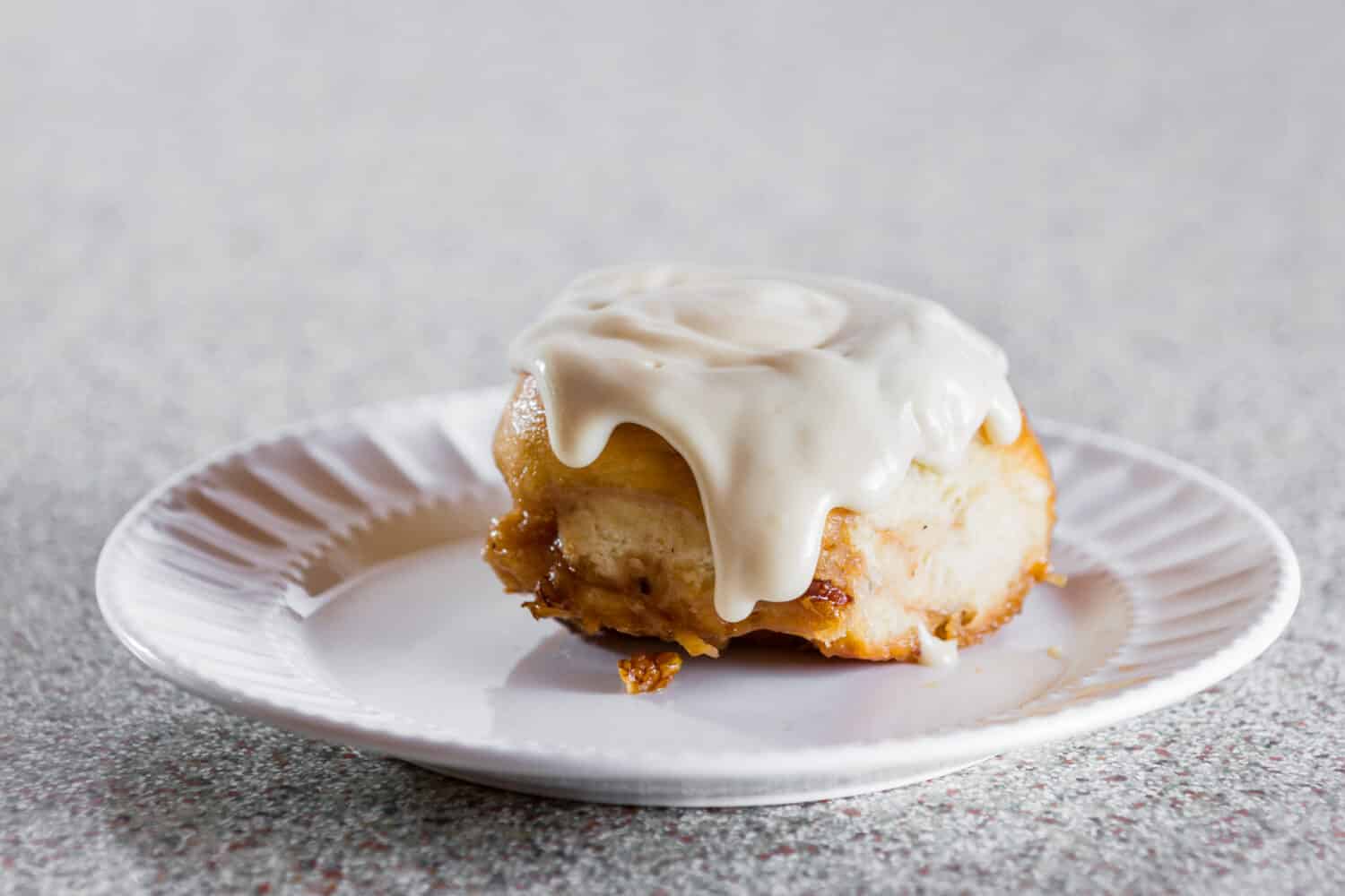 Close up of a home made cinnamon roll served on a white plate with a cream cheese frosting on top