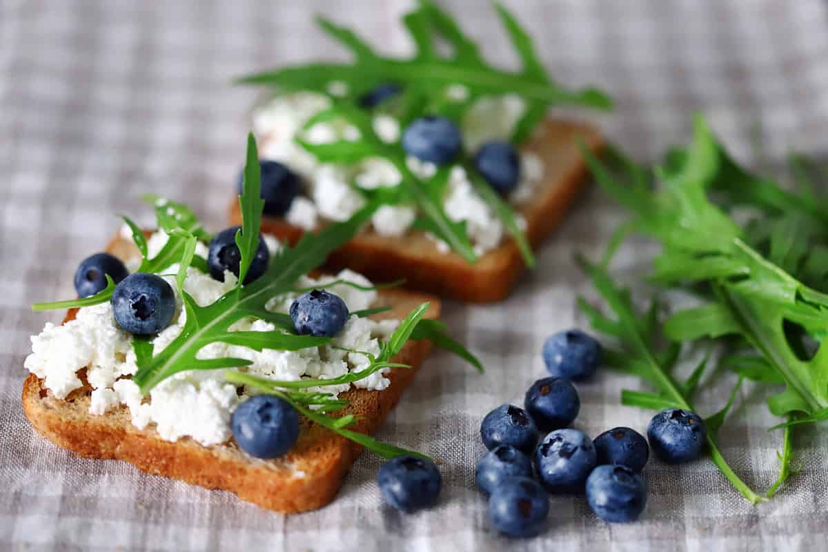 Selective focus. Cottage cheese toast with blueberries and arugula. The keto diet. Keto toast. Bruschetta with cottage cheese.