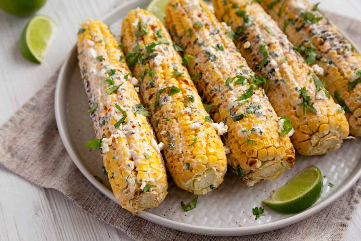 Homemade Elote Mexican Street Corn on a plate on a white wooden background, side view. Close-up.