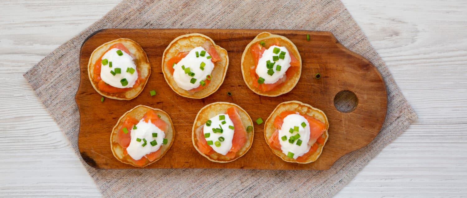 Homemade Blini with Smoked Salmon, Creme and Chives on a rustic wooden board, top view. Flat lay, overhead, from above. 