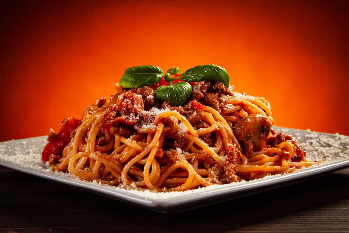 Spaghetti with marinara sauce, meat and parmesan on wooden table against gradient orange background