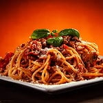 Spaghetti with marinara sauce, meat and parmesan on wooden table against gradient orange background