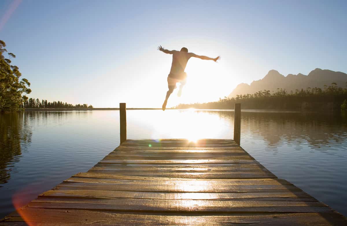 Horizontal rear view of a man leaping from a jetty into the lake at sunset.