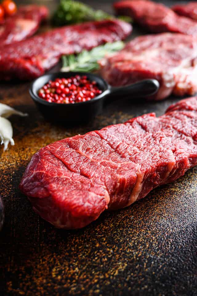 Side view Close up denver Steak, Flank steak, cut near denver alternative beef steak and a cleaver butcher meat knife a rustic metall background vertical