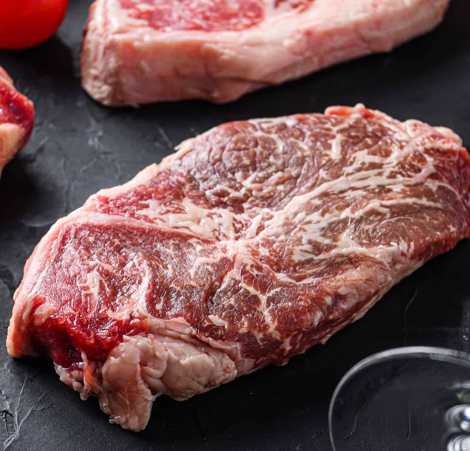 Flat Iron beef steak cuts, with herbs, seasoning on black table, side view