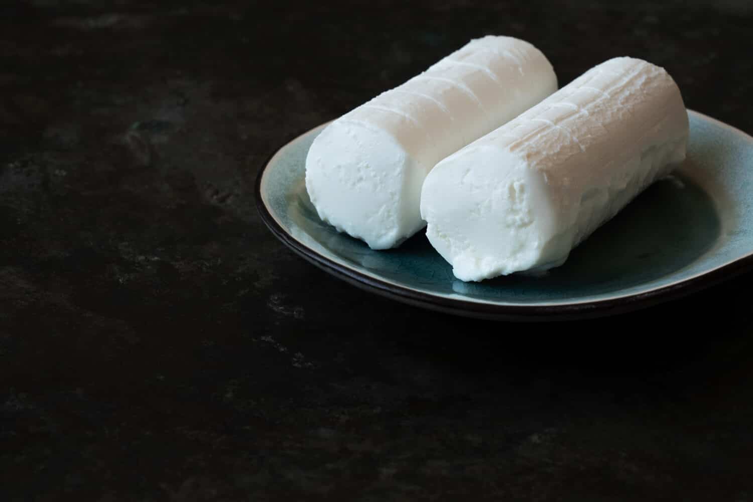 French goat Cheese, soft cheese, traditional appetizer, snack, dessert on ceramic plate over a rustic metal background.