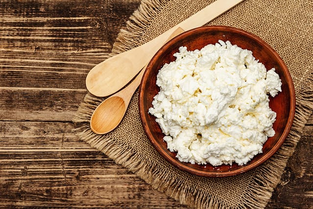 Organic homemade cottage cheese or curd in bowl on wooden rustic background, top view
