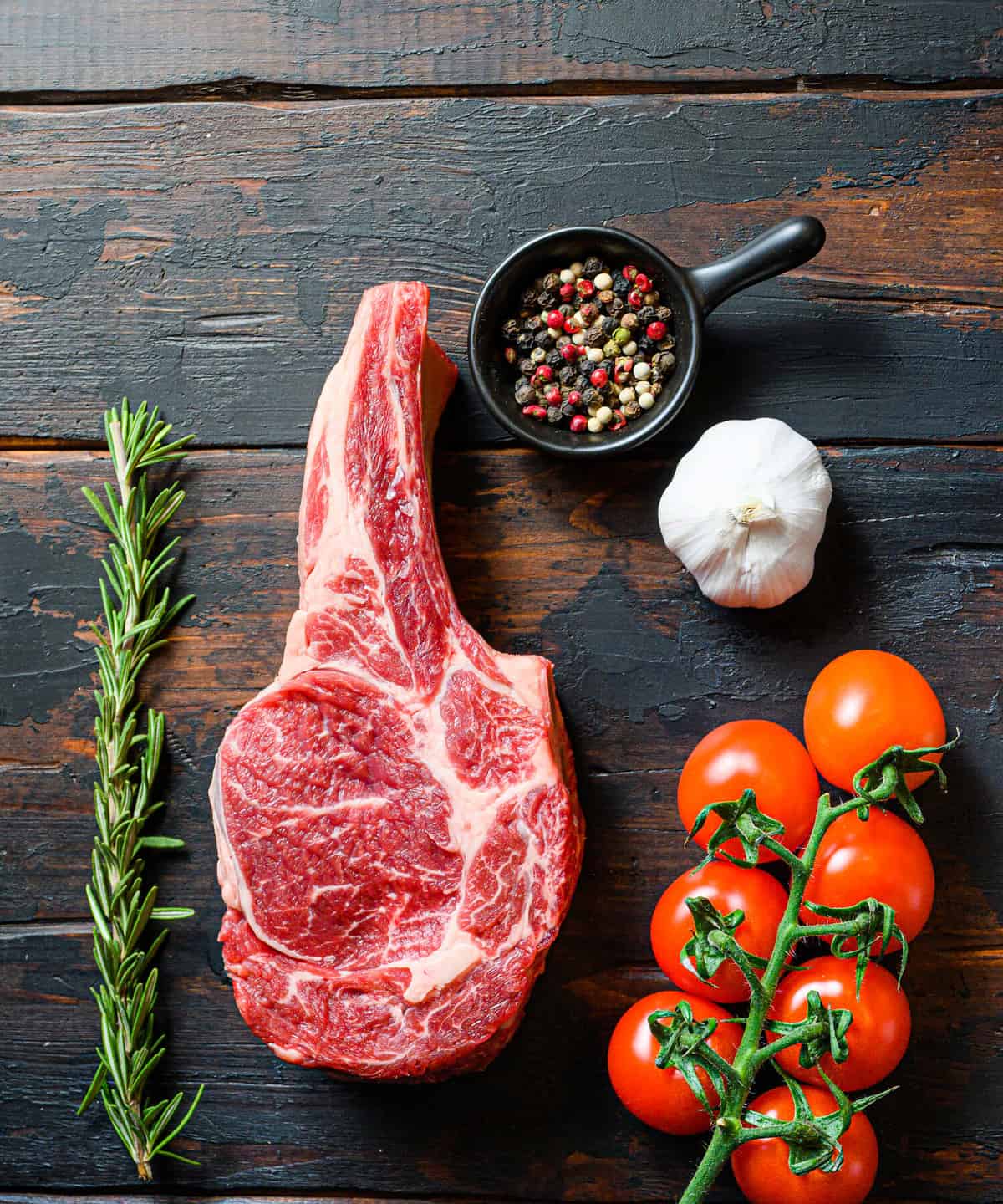 Raw uncooked black angus beefmarket steak closeup with tomatoes garlic herbs and peppercorns rosemary on wooden dark old rustic table planks