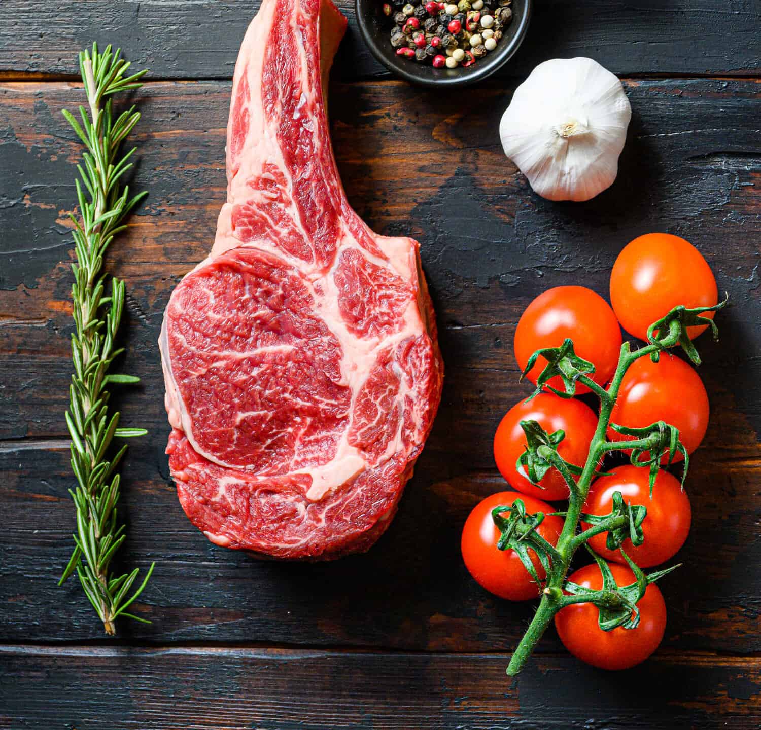 Raw uncooked black angus beefmarket steak closeup with tomatoes garlic herbs and peppercorns rosemary on wooden dark old rustic table planks