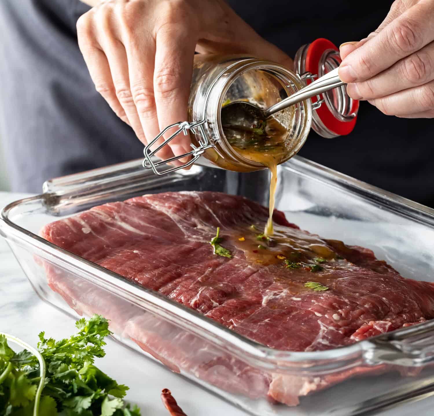 Close up of a chef's hands pouring marinade on a flank of raw beef.
