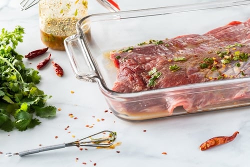 Flank of steak covered in homemade lime and cilantro marinade in a glass dish.