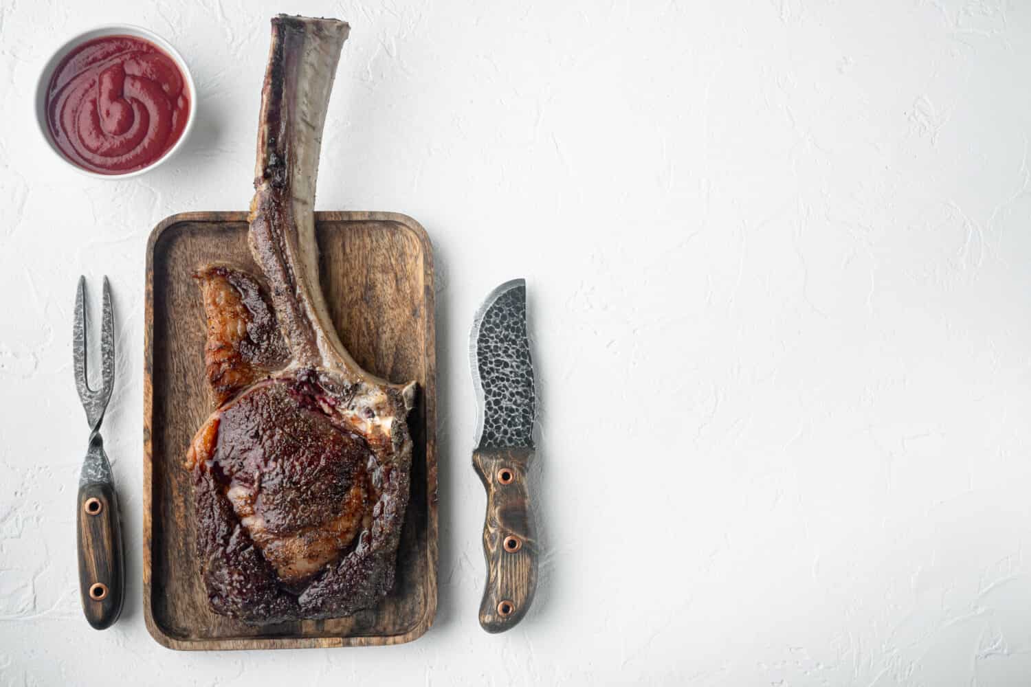 Grilled tomahawk beef steak set, on wooden serving board, on white stone background, top view flat lay, with copy space for text