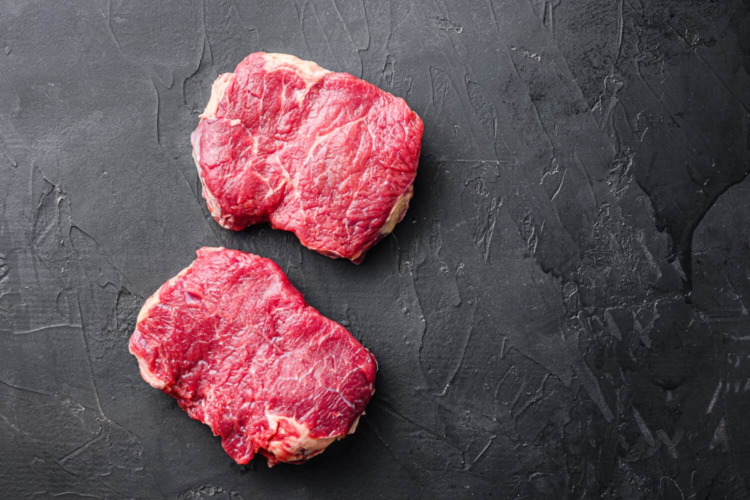 Fresh beef Rump steaks over black background, top view with space for text