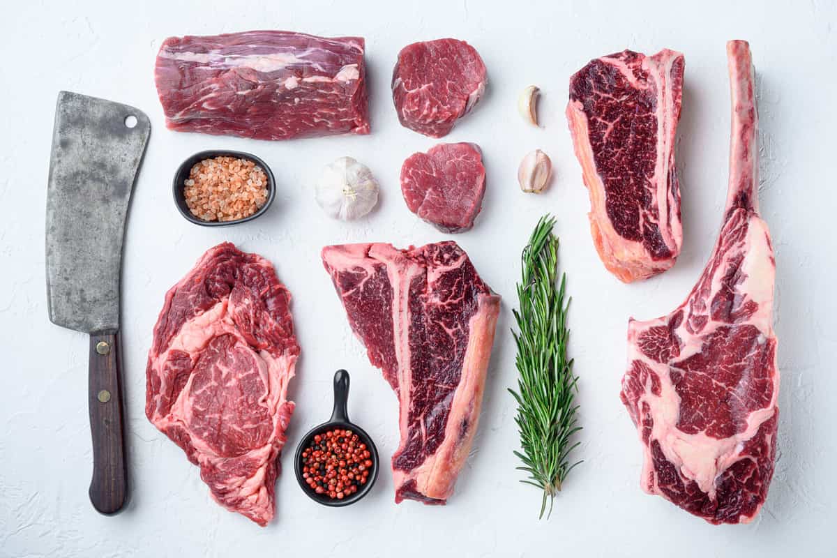 Marbled beef meat steak cut set, tomahawk, t bone, club steak, rib eye and tenderloin cuts, on white stone background, top view flat lay