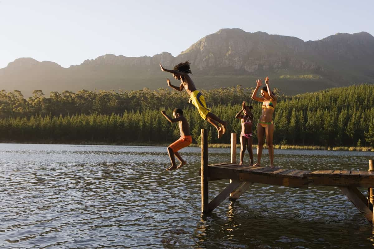 Family, in swimwear, standing on jetty, father and son (8-10) jumping into lake, side view