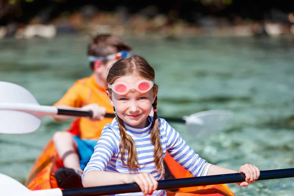 Kids enjoying paddling in colorful red kayak at tropical ocean water during summer vacation