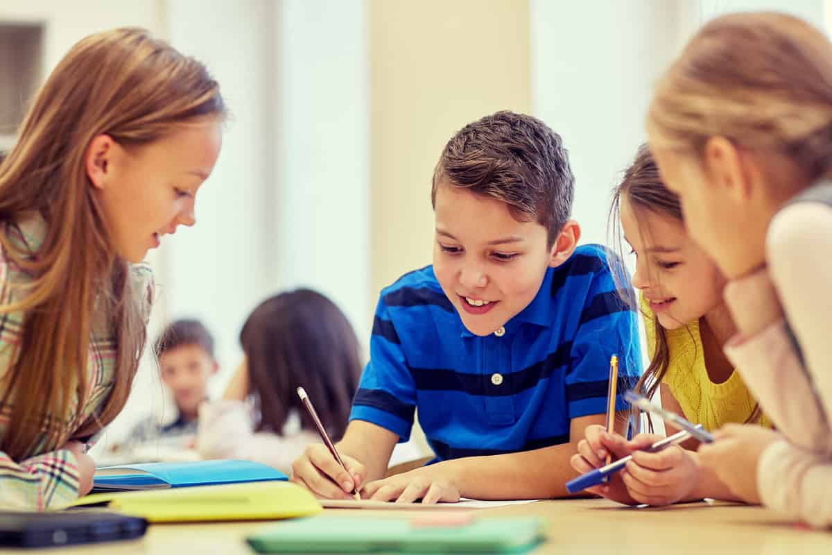 Photo of young middle school students on a table taking on an assignment together.